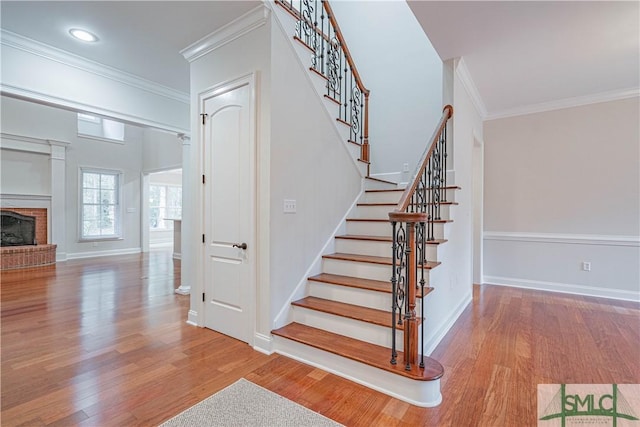 stairway featuring a fireplace, wood-type flooring, and crown molding