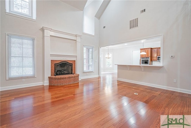 unfurnished living room with a chandelier, a high ceiling, light wood-type flooring, and a brick fireplace