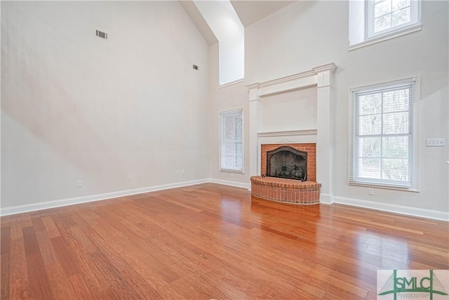 unfurnished living room featuring a towering ceiling, a fireplace, and light hardwood / wood-style flooring