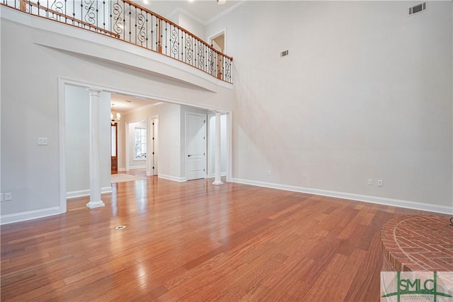 unfurnished living room with ornate columns, an inviting chandelier, ornamental molding, a towering ceiling, and hardwood / wood-style flooring