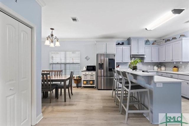 kitchen with stainless steel fridge, gray cabinetry, a kitchen breakfast bar, a kitchen island, and pendant lighting