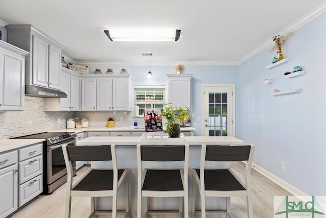 kitchen featuring stainless steel range with electric stovetop, gray cabinets, a breakfast bar area, backsplash, and crown molding