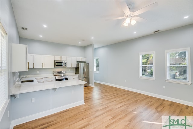 kitchen featuring kitchen peninsula, white cabinets, appliances with stainless steel finishes, a kitchen bar, and light hardwood / wood-style floors