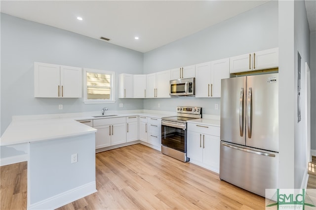 kitchen featuring appliances with stainless steel finishes, sink, light wood-type flooring, kitchen peninsula, and white cabinetry