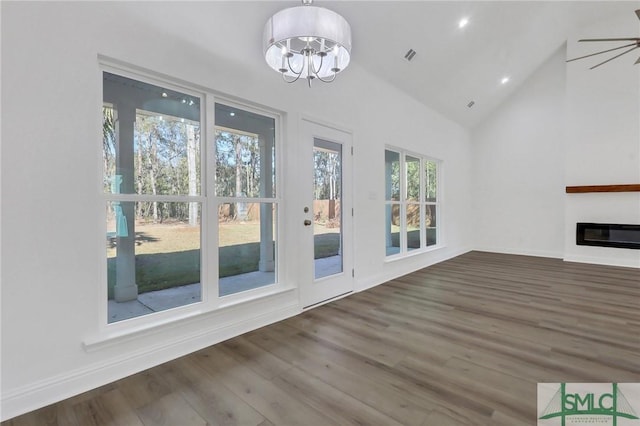 unfurnished living room with ceiling fan with notable chandelier, wood-type flooring, and vaulted ceiling