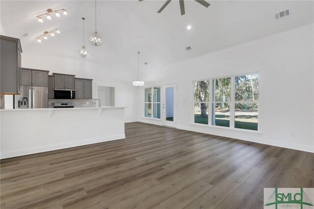 unfurnished living room featuring dark hardwood / wood-style flooring, a towering ceiling, ceiling fan with notable chandelier, and sink