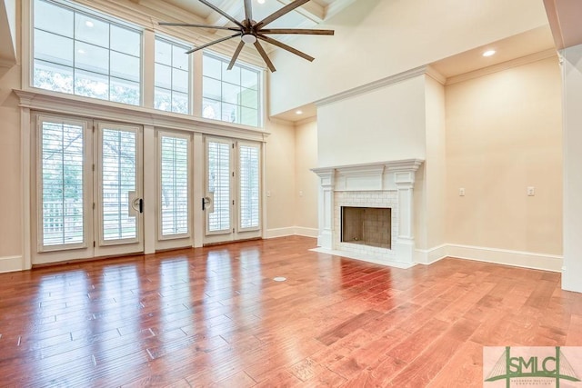 unfurnished living room with ornamental molding, ceiling fan, a fireplace, hardwood / wood-style floors, and a high ceiling