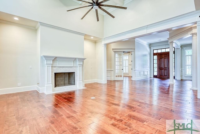 unfurnished living room with ornate columns, crown molding, a brick fireplace, and hardwood / wood-style flooring