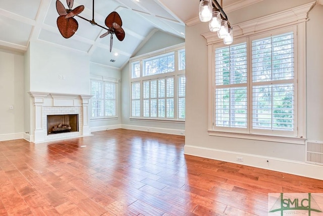 unfurnished living room with ceiling fan, wood-type flooring, a tiled fireplace, and lofted ceiling with beams