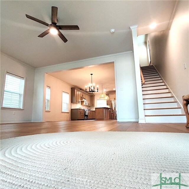 unfurnished living room with ornamental molding, light wood-type flooring, and ceiling fan with notable chandelier