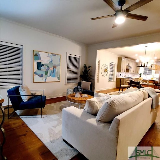 living area featuring ornamental molding, wood finished floors, and ceiling fan with notable chandelier