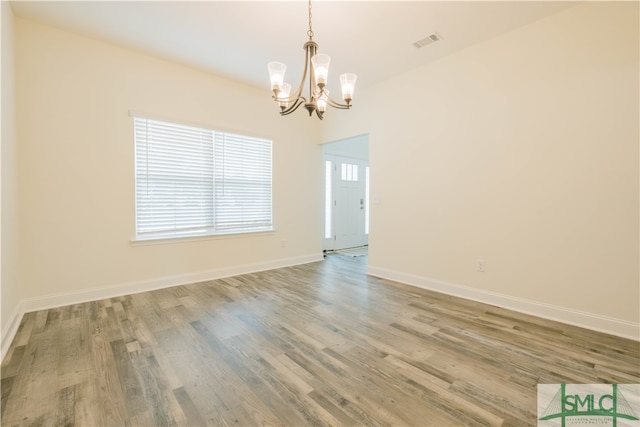 empty room with a notable chandelier and hardwood / wood-style floors