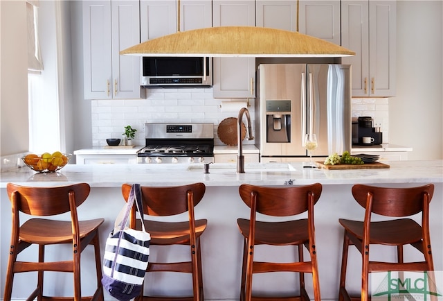 kitchen featuring a kitchen island with sink, light stone counters, stainless steel appliances, and backsplash