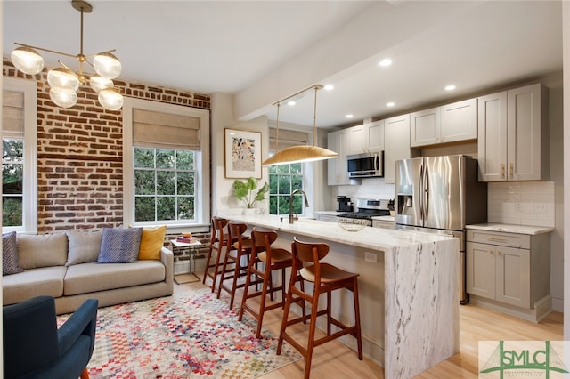 kitchen with decorative backsplash, appliances with stainless steel finishes, light wood-type flooring, and a kitchen bar