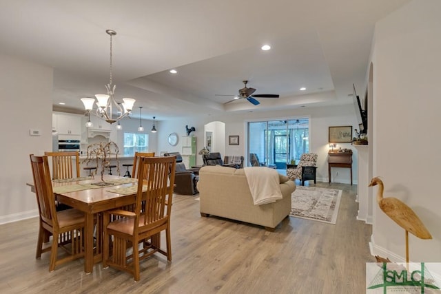 dining room featuring ceiling fan with notable chandelier, light hardwood / wood-style floors, and a raised ceiling