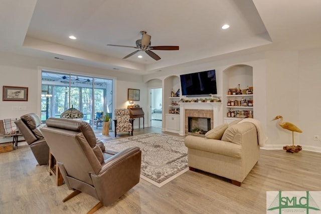 living room featuring a tray ceiling, built in features, and ceiling fan