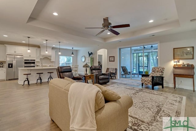 living room featuring light hardwood / wood-style flooring, a raised ceiling, ceiling fan, and sink