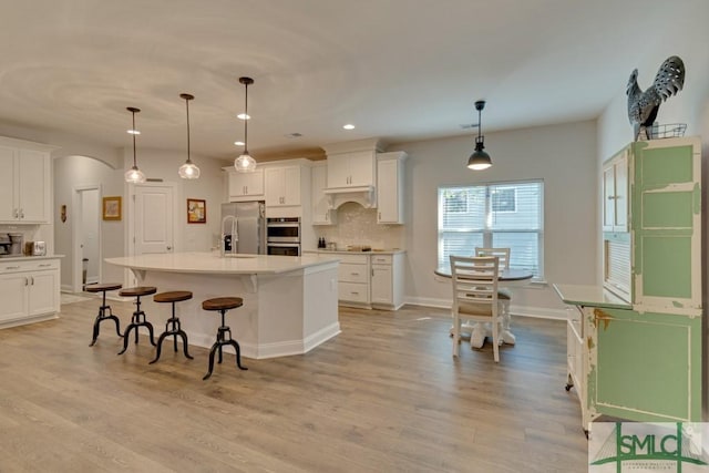 kitchen featuring backsplash, a kitchen island with sink, white cabinets, and pendant lighting