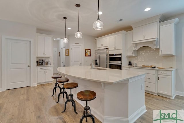 kitchen featuring a kitchen island with sink, white cabinets, sink, hanging light fixtures, and appliances with stainless steel finishes