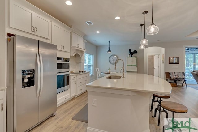 kitchen with stainless steel appliances, plenty of natural light, decorative light fixtures, a kitchen island with sink, and white cabinets