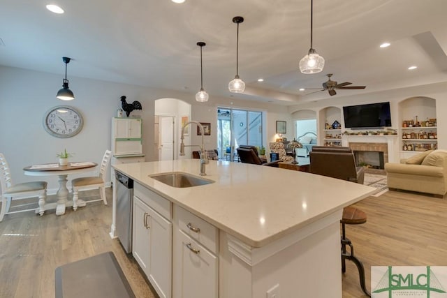 kitchen featuring white cabinets, decorative light fixtures, a center island with sink, and sink