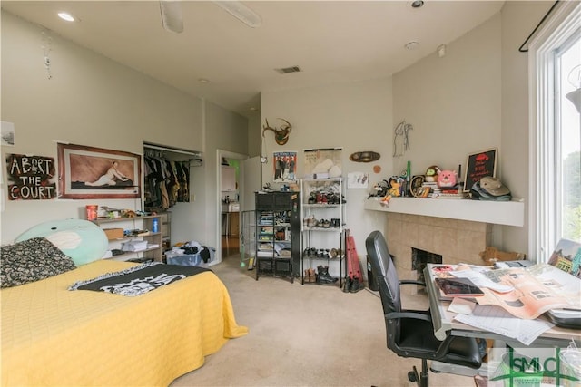 bedroom with light carpet, a fireplace, ceiling fan, and a closet