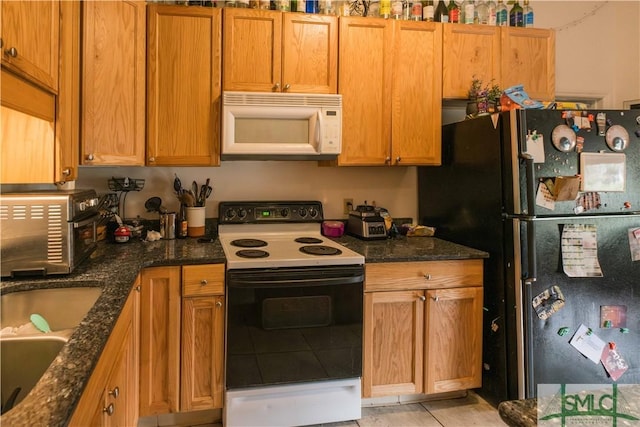 kitchen featuring range with electric stovetop, black refrigerator, sink, dark stone counters, and light tile patterned floors