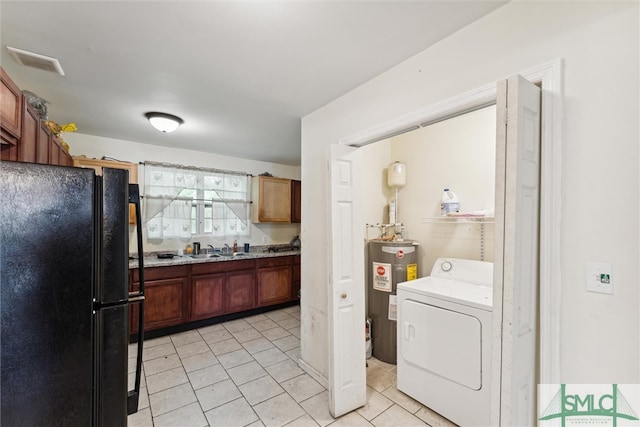 kitchen featuring electric water heater, black fridge, sink, washer / dryer, and light tile patterned floors