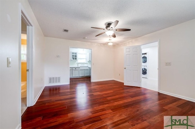 interior space with dark hardwood / wood-style floors, ceiling fan, stacked washing maching and dryer, and a textured ceiling