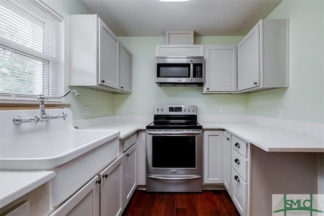 kitchen featuring dark wood-type flooring, white cabinetry, stainless steel appliances, and a textured ceiling