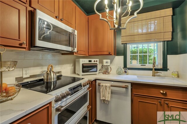 kitchen with light stone countertops, stainless steel appliances, sink, backsplash, and a notable chandelier