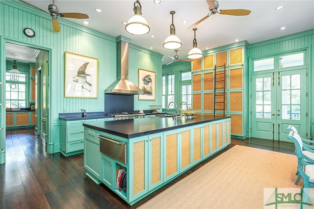 kitchen featuring sink, wall chimney range hood, dark hardwood / wood-style flooring, hanging light fixtures, and a kitchen island with sink