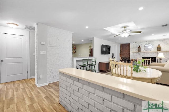 interior space featuring light wood-type flooring, ceiling fan, brick wall, and a brick fireplace