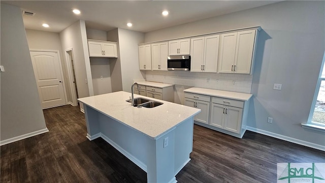 kitchen featuring sink, white cabinets, backsplash, a kitchen island with sink, and dark wood-type flooring