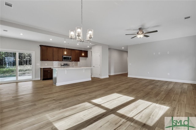 kitchen featuring pendant lighting, a center island with sink, ceiling fan with notable chandelier, sink, and light wood-type flooring