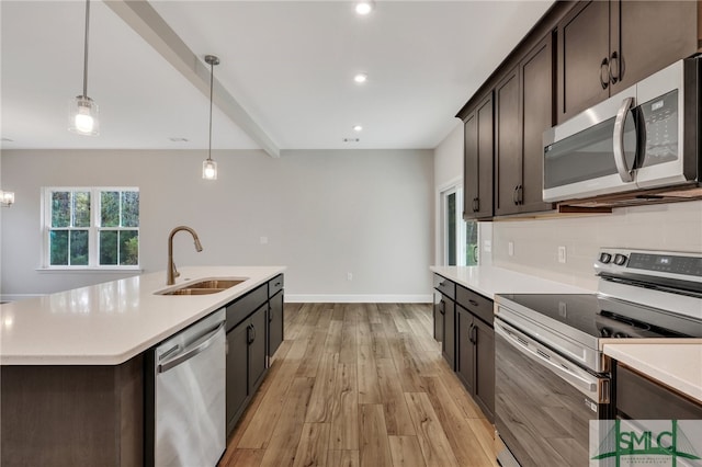 kitchen with light wood-type flooring, stainless steel appliances, a kitchen island with sink, sink, and pendant lighting