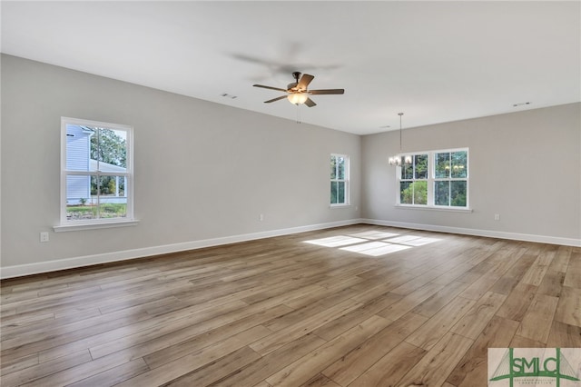 spare room featuring a healthy amount of sunlight, ceiling fan with notable chandelier, and light hardwood / wood-style floors