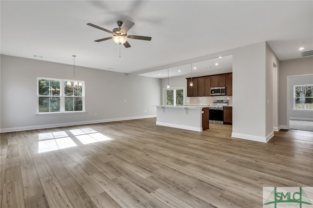 unfurnished living room with plenty of natural light, light wood-type flooring, and ceiling fan with notable chandelier