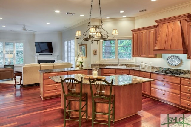 kitchen featuring visible vents, a center island, premium range hood, a fireplace, and a sink