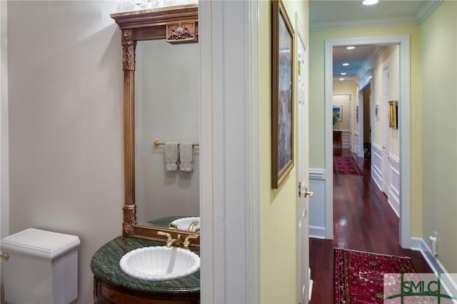 hallway with a wainscoted wall, crown molding, recessed lighting, dark wood-type flooring, and a sink