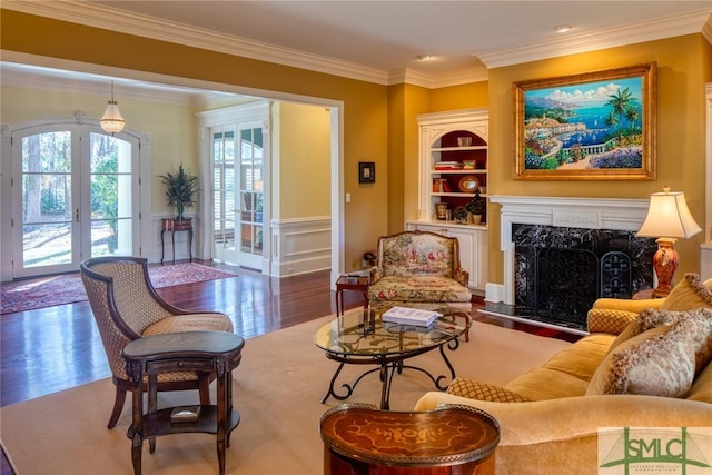 sitting room with built in features, wood finished floors, a high end fireplace, and crown molding