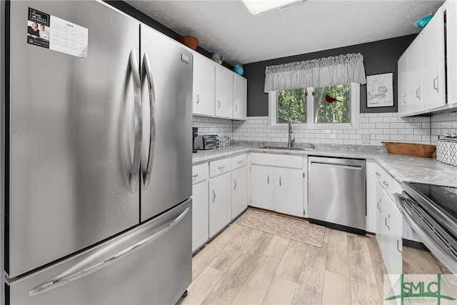 kitchen with white cabinetry, sink, decorative backsplash, light hardwood / wood-style floors, and stainless steel appliances