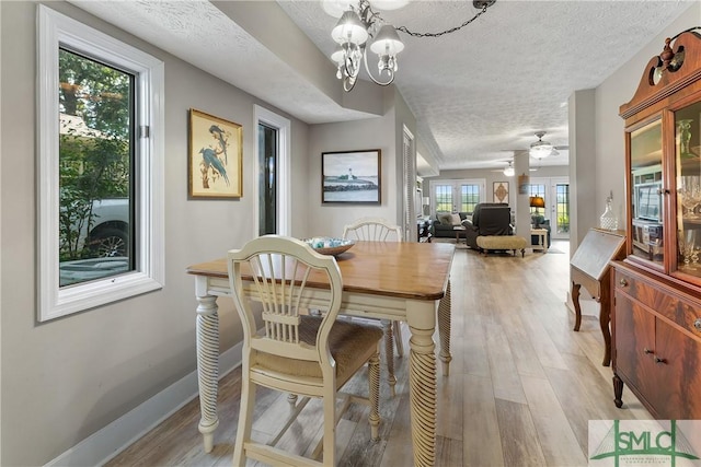 dining space with ceiling fan with notable chandelier, light hardwood / wood-style flooring, and a textured ceiling