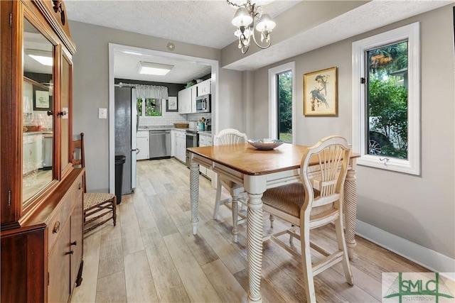 dining area featuring a chandelier, a textured ceiling, and light wood-type flooring