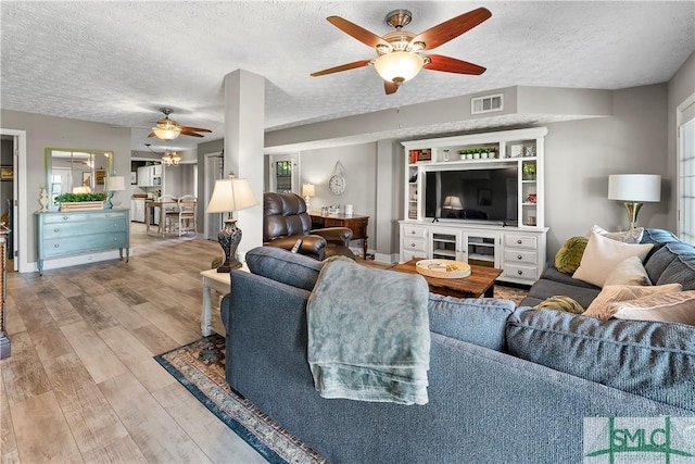 living room featuring ceiling fan, a textured ceiling, and light wood-type flooring