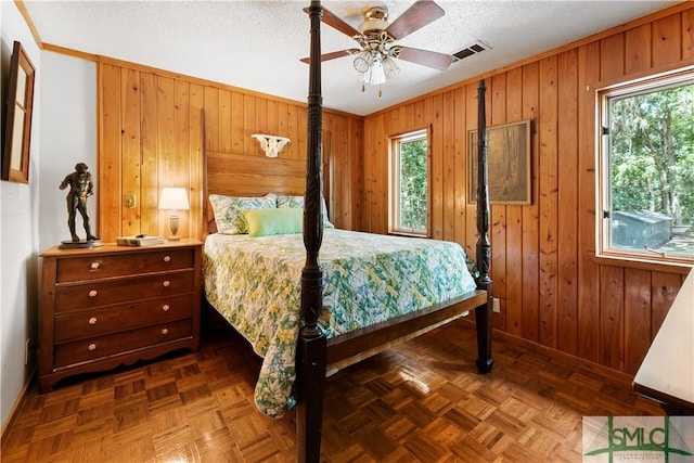 bedroom featuring wood walls, parquet floors, ornamental molding, ceiling fan, and a textured ceiling