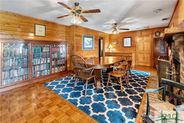 dining room with ceiling fan, a textured ceiling, light parquet floors, and wood walls