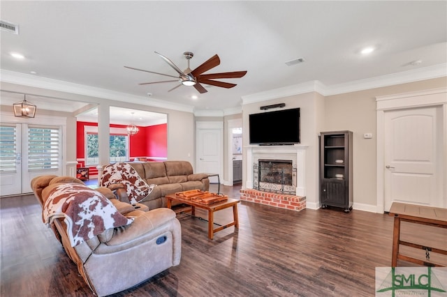 living room featuring a fireplace, ceiling fan with notable chandelier, crown molding, french doors, and dark wood-type flooring