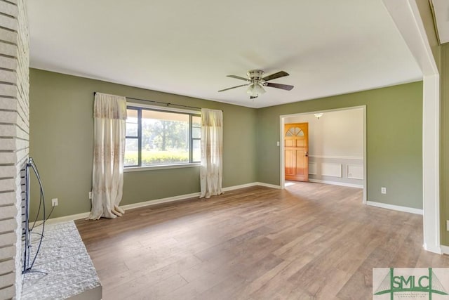 unfurnished living room with ceiling fan, a brick fireplace, and light wood-type flooring