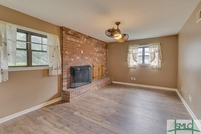 unfurnished living room with wood-type flooring and a brick fireplace